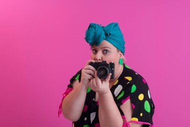 Artı, komik duygusal yüz ifadesi olan, pembe arka planda izole edilmiş kot elbiseli klasik kameralı, gülümseyen kadın, tatilde gezgin, yaz modası tarzı, heyecanlı turist..