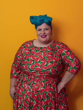 Moda makyajlı, komik, seksi model bir kadın. Stüdyoda sarı arka planda poz veren, şık, şişman, renkli elbiseli bir sarışın..