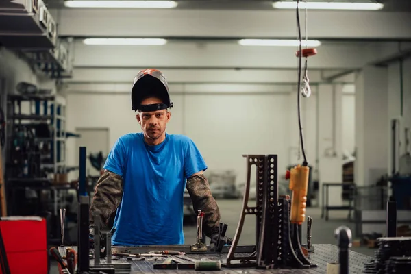 年轻专业重工工程师的肖像.工人穿着安全背心，头戴安全帽，在相机上微笑。背景下的无重点大型工业厂房 — 图库照片