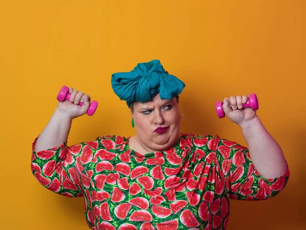 Fat woman dieting, fitness and health at home.Big woman and sport. Healthy, fitness and sports concept. Plus size young woman doing exercise with dumbbells on yellow background. — Fotografia de Stock