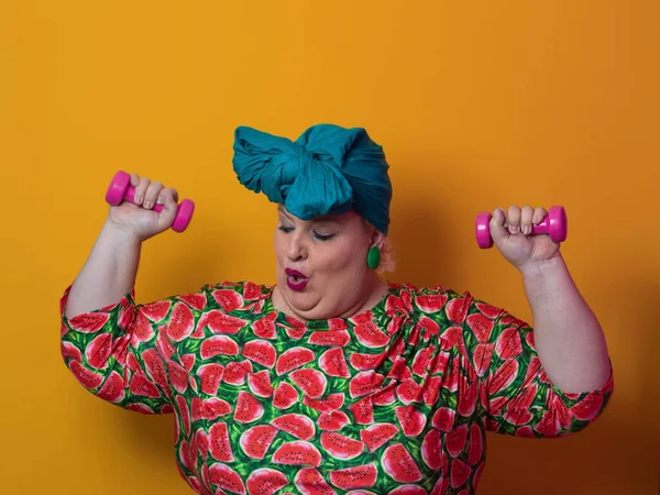 Fat woman dieting, fitness and health at home.Big woman and sport. Healthy, fitness and sports concept. Plus size young woman doing exercise with dumbbells on yellow background. — Stock Photo, Image
