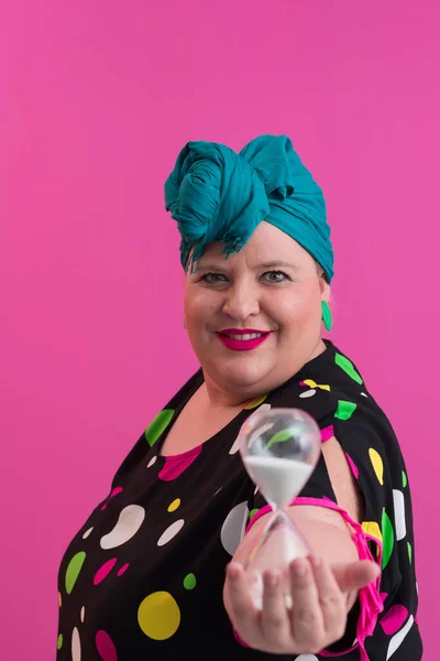 Ritratto di plus size giovane signora sorridente mani tiene orologio di sabbia isolato su sfondo di colore rosa. — Foto Stock