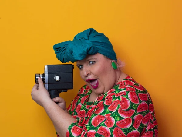 Plus size smiling woman with funny emotional face expression with vintage camera in dress isolated on yellow background, traveler on vacation, summer fashion style, excited tourist. — Stock Photo, Image