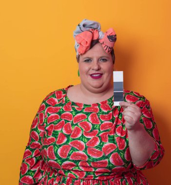 Moda makyajlı, komik, seksi model bir kadın. Stüdyoda sarı arka planda poz veren, şık, şişman, renkli elbiseli bir sarışın..