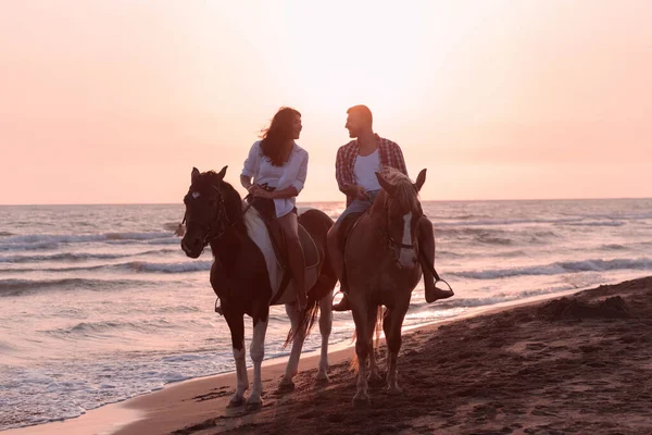 A loving young couple in summer clothes riding a horse on a sandy beach at sunset. Sea and sunset in the background. Selective focus — Φωτογραφία Αρχείου