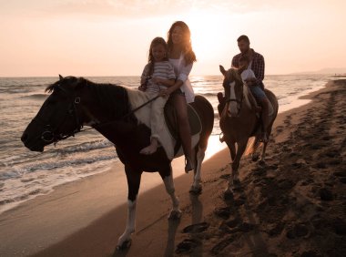Aile kumlu bir sahilde birlikte ata binerken çocuklarıyla vakit geçirir. Seçici odak 