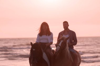 a loving couple in summer clothes riding a horse on a sandy beach at sunset. Sea and sunset in the background. Selective focus 