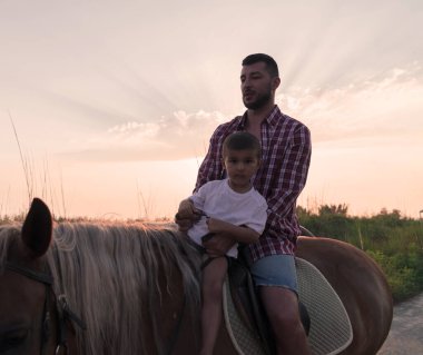 Father and son enjoy riding horses together by the sea. Selective focus 