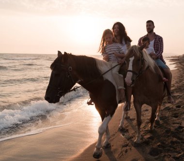 Aile kumlu bir sahilde birlikte ata binerken çocuklarıyla vakit geçirir. Seçici odak 