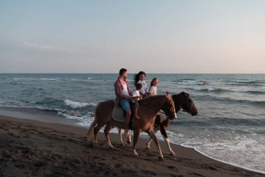 Aile kumlu bir sahilde birlikte ata binerken çocuklarıyla vakit geçirir. Seçici odak 