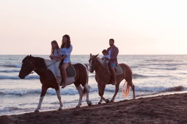 Aile kumlu bir sahilde birlikte ata binerken çocuklarıyla vakit geçirir. Seçici odak 