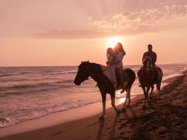 The family spends time with their children while riding horses together on a sandy beach. Selective focus 