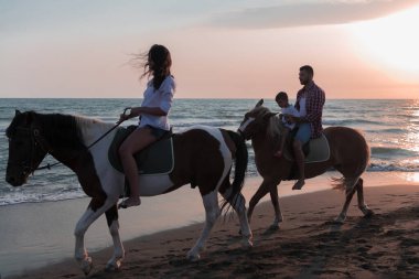 The family spends time with their children while riding horses together on a sandy beach. Selective focus 
