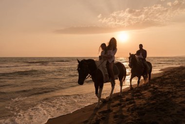 The family spends time with their children while riding horses together on a sandy beach. Selective focus 