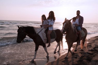Aile kumlu bir sahilde birlikte ata binerken çocuklarıyla vakit geçirir. Seçici odak 