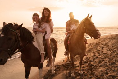 Aile kumlu bir sahilde birlikte ata binerken çocuklarıyla vakit geçirir. Seçici odak 