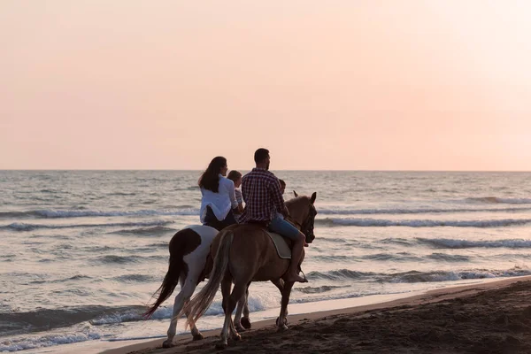 The family spends time with their children while riding horses together on a sandy beach. Selective focus — Fotografia de Stock