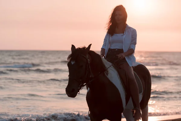 Femme en vêtements d'été aime monter à cheval sur une belle plage de sable au coucher du soleil. Concentration sélective — Photo