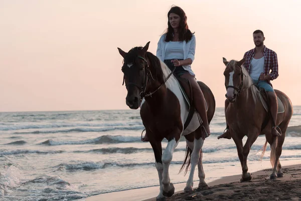 A loving couple in summer clothes riding a horse on a sandy beach at sunset. Sea and sunset in the background. Selective focus — Foto de Stock