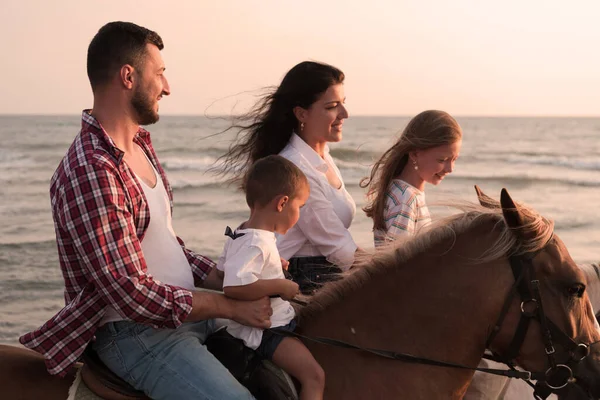 The family spends time with their children while riding horses together on a sandy beach. Selective focus —  Fotos de Stock