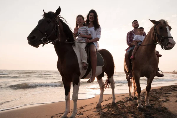 The family spends time with their children while riding horses together on a sandy beach. Selective focus —  Fotos de Stock