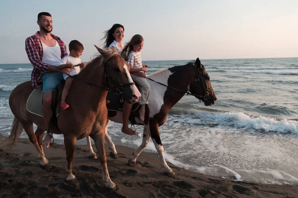 The family spends time with their children while riding horses together on a sandy beach. Selective focus — 图库照片