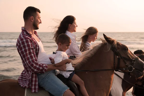 The family spends time with their children while riding horses together on a sandy beach. Selective focus — Stockfoto