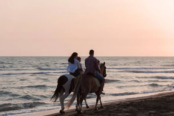 La famille passe du temps avec ses enfants tout en chevauchant des chevaux ensemble sur une plage de sable fin. Concentration sélective — Photo
