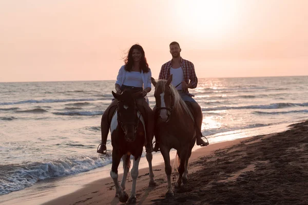 Любляча пара в літньому одязі катається на коні на піщаному пляжі на заході сонця. Море і захід сонця на задньому плані. Вибірковий фокус — стокове фото