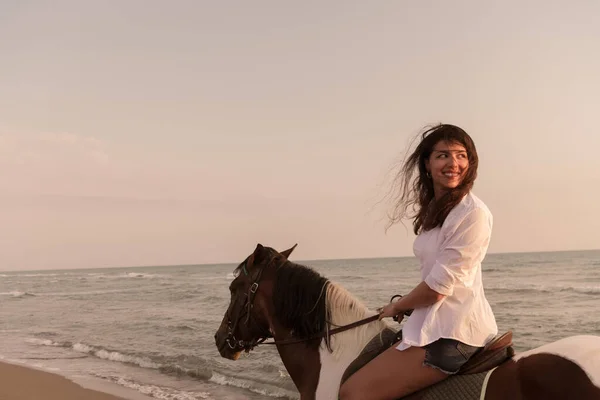夏の服の女性は、日没時に美しい砂浜で馬に乗るのを楽しんでいます。選択的焦点 — ストック写真