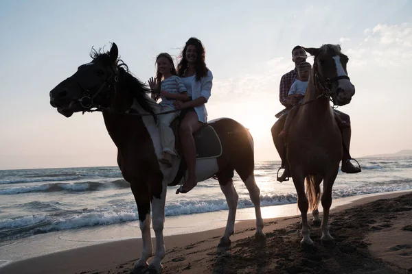 The family spends time with their children while riding horses together on a sandy beach. Selective focus — Zdjęcie stockowe