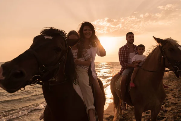 The family spends time with their children while riding horses together on a sandy beach. Selective focus — Stok fotoğraf