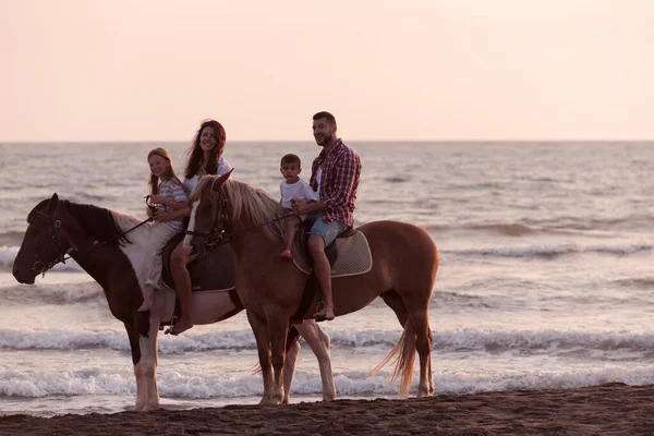 The family spends time with their children while riding horses together on a sandy beach. Selective focus — Stok fotoğraf