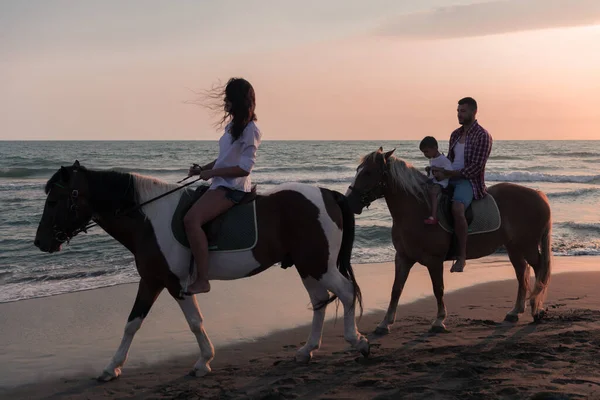 The family spends time with their children while riding horses together on a sandy beach. Selective focus — Foto de Stock