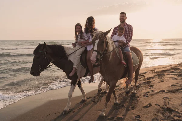 The family spends time with their children while riding horses together on a sandy beach. Selective focus — Stock Fotó