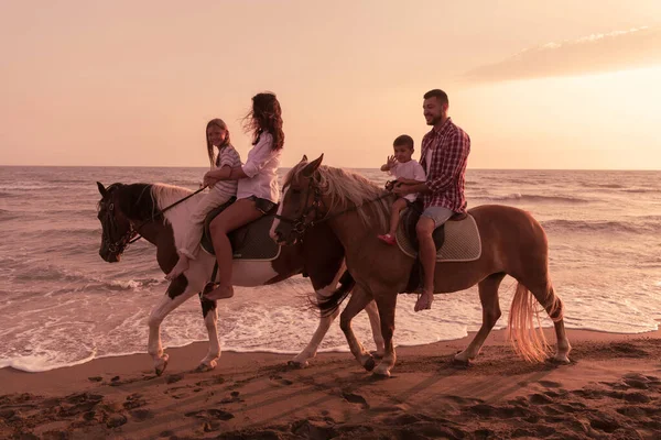 The family spends time with their children while riding horses together on a sandy beach. Selective focus — Zdjęcie stockowe