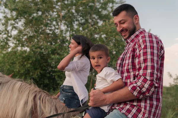 The family spends time with their children while riding horses together on a forest road. Selective focus — Fotografia de Stock