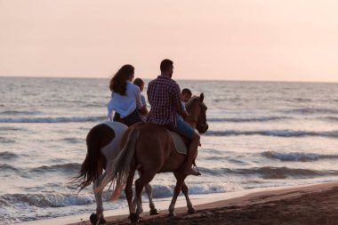 The family spends time with their children while riding horses together on a sandy beach. Selective focus 