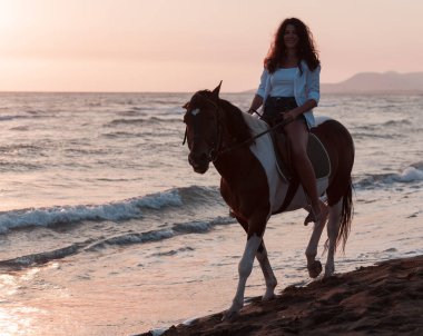 Yaz kıyafetleri içinde bir kadın gün batımında kumlu güzel bir sahilde ata binmekten hoşlanır. Seçici odak 