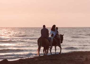 The family spends time with their children while riding horses together on a sandy beach. Selective focus 