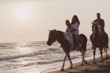 The family spends time with their children while riding horses together on a sandy beach. Selective focus 