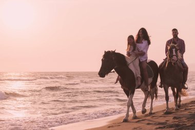 The family spends time with their children while riding horses together on a sandy beach. Selective focus 