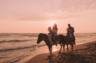 The family spends time with their children while riding horses together on a sandy beach. Selective focus 