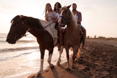 Aile kumlu bir sahilde birlikte ata binerken çocuklarıyla vakit geçirir. Seçici odak 