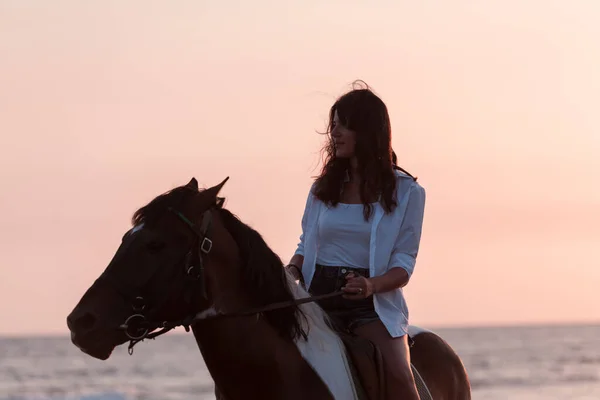 Frau in Sommerkleidung genießt es, bei Sonnenuntergang auf einem Pferd an einem schönen Sandstrand zu reiten. Selektiver Fokus — Stockfoto