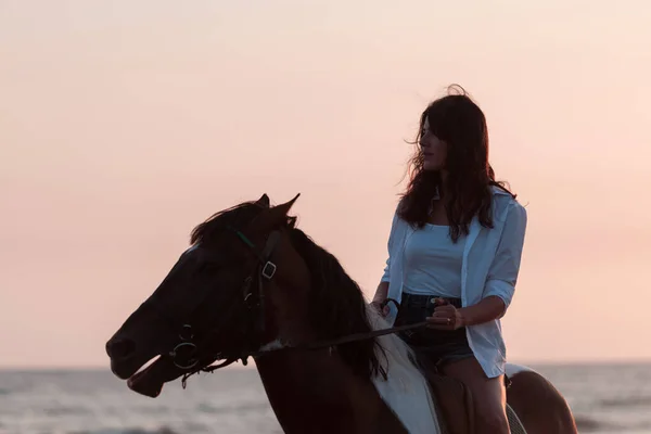 Kvinnan i sommarkläder njuter av att rida på en häst på en vacker sandstrand vid solnedgången. Selektiv inriktning — Stockfoto