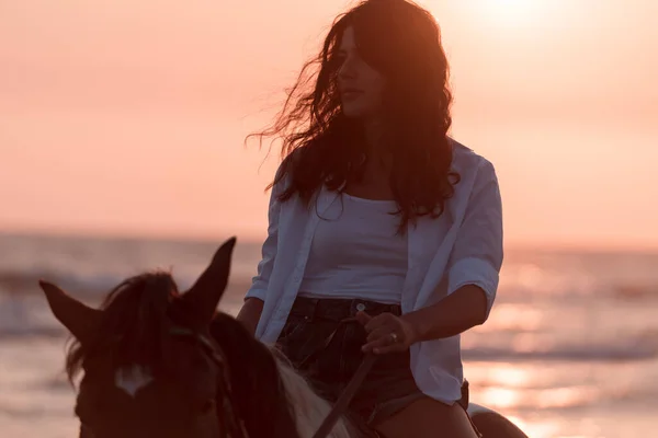Žena v letním oblečení si užívá jízdu na koni na krásné písečné pláži při západu slunce. Selektivní zaměření — Stock fotografie