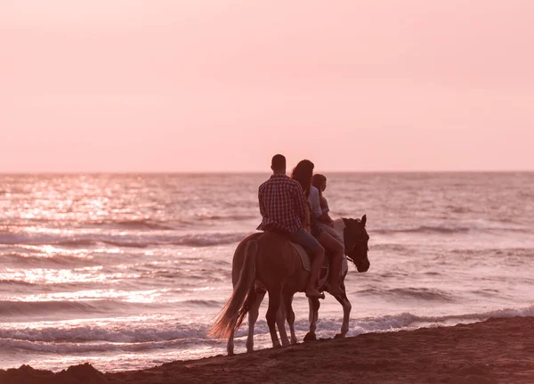 De familie brengt tijd door met hun kinderen terwijl ze samen paardrijden op een zandstrand. Selectieve focus — Stockfoto