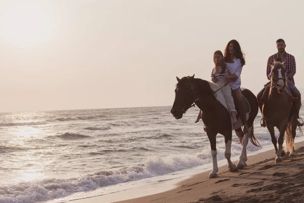 The family spends time with their children while riding horses together on a sandy beach. Selective focus — Stok fotoğraf