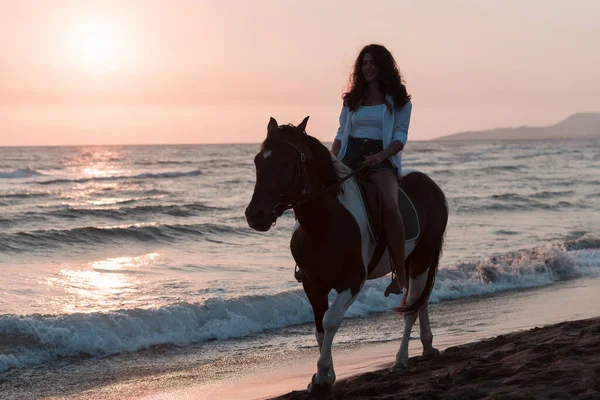 Mujer en ropa de verano disfruta montar a caballo en una hermosa playa de arena al atardecer. Enfoque selectivo — Foto de Stock